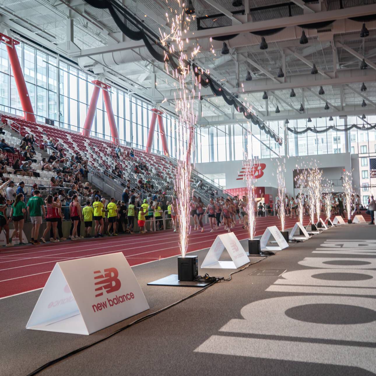 A New Balance track event with people in the stands and sparklers spraying into the air.